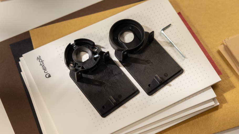 Deux composants en plastique noir pour un Nuki Smart Lock Pro sur une pile de papiers, avec un outil en L à côté.
