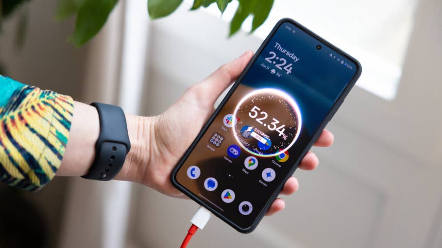 Une personne tient un smartphone OnePlus 13R affichant lu0027heure et lu0027état de la batterie, branché à un chargeur.