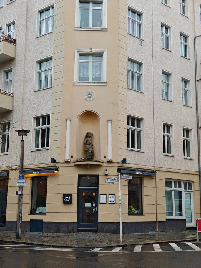 Un coin de bâtiment avec une statue ornée, de grandes fenêtres et un panneau pour le café u0027nomadu0027.