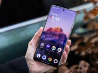 Une personne tenant un smartphone OnePlus 13 affichant l'écran d'accueil avec l'heure et les applications.