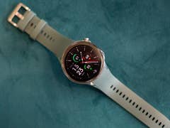 La OnePlus Watch 2 vue de face et de haut, posée avec son bracelet déroulé à plat sur une surface verte