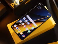 Le Poco X6 Pro vu du dessus et posé sur sa boîte jaune sur une table avec son écran allumé.