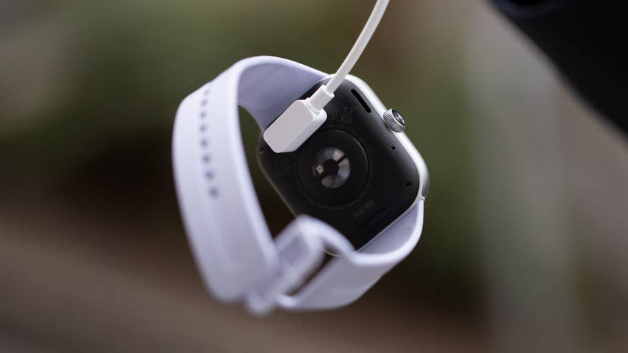 Une Redmi Watch 5 en charge avec un bracelet blanc et un connecteur magnétique visible.