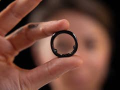 Une personne tient une bague intelligente RingConn devant son visage sur un fond sombre.
