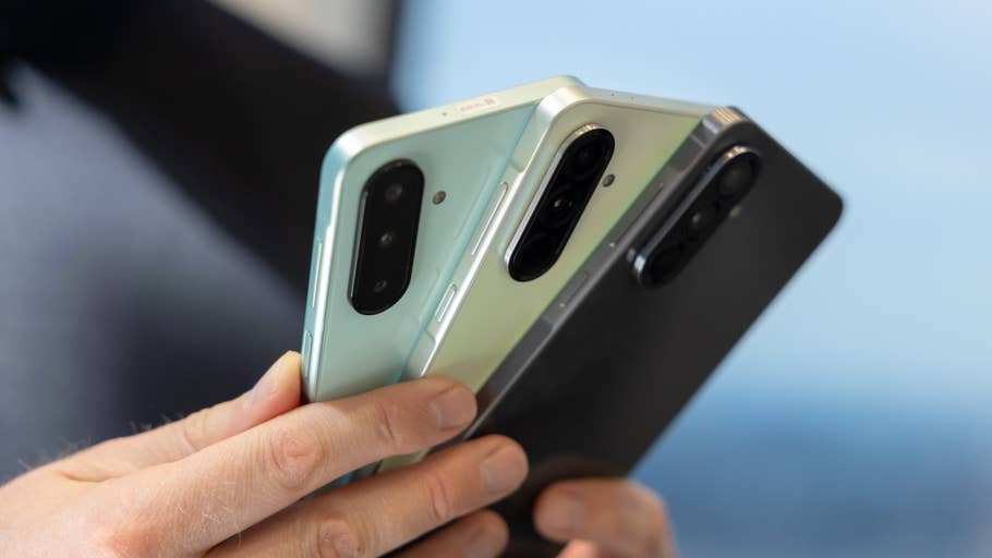 Trois smartphones de la série Samsung Galaxy A tenus par une personne, montrant différentes couleurs et conceptions de caméra.