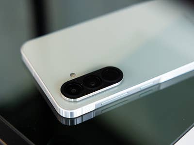 Un smartphone Samsung Galaxy A56 posé sur une surface en verre montre son module photo et son design.