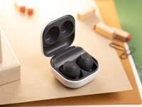 Samsung Galaxy Buds FE dans leur étui de chargement, posés sur une surface texturée.