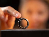 Un gros plan d'une bague Samsung Galaxy sur un support, avec une main s'approchant pour la toucher en arrière-plan.