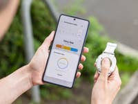 Personne tenant une Samsung Galaxy Watch 8 Classic tout en vérifiant l'indice d'antioxydants sur un smartphone.