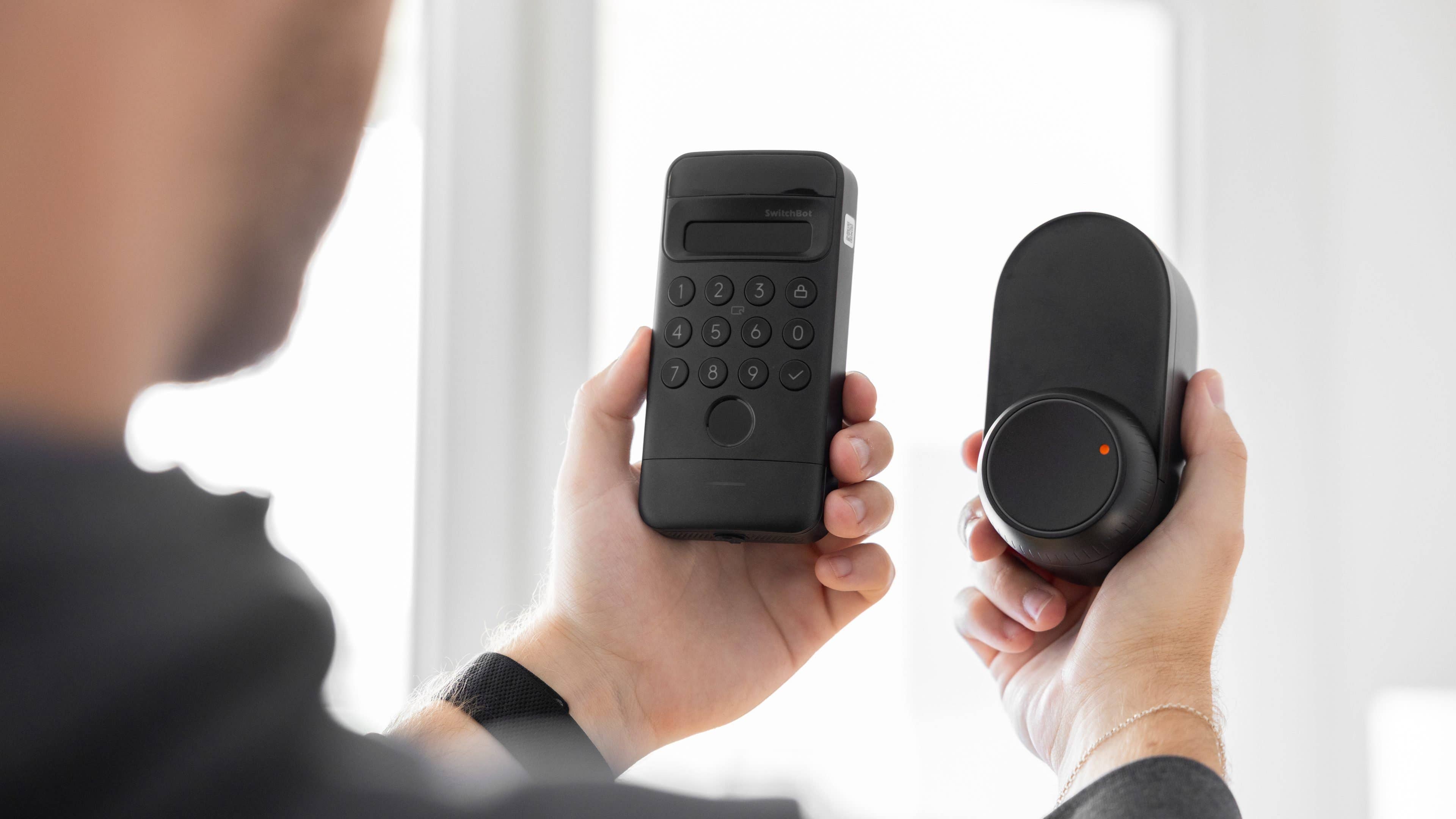 nextpit_SwitchBot_Lock_Ultra_Touch_Combo_Test.jpg Une personne tient un verrou à clavier SwitchBot Ultra Touch et un appareil de verrouillage intelligent dans les mains.