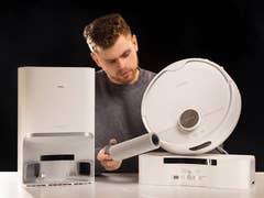 Un homme examine l'aspirateur robot SwitchBot S10 et sa station d'accueil.