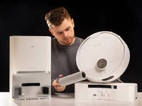 Un homme examine l'aspirateur robot SwitchBot S10 et sa station d'accueil.