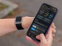 Une personne tenant un smartphone affichant l'application Whoop, avec un tracker de fitness à son poignet.