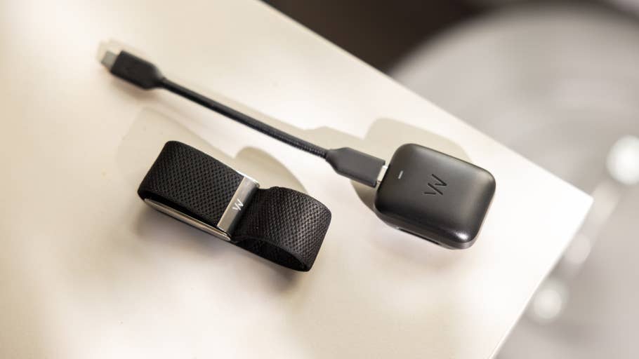 Un appareil noir portable avec un bandeau et un câble de chargeur posés sur une surface blanche.