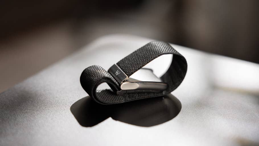Un bracelet de matériau noir pilé sur une boucle en métal posé sur une surface sombre.