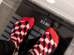 Des pieds avec des chaussettes à motifs rouges et blancs sur une balance Withings Body Scan affichant 62,80 kg.