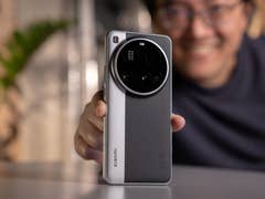 Une personne tient un smartphone Xiaomi 15 Ultra, souriant avec de la verdure en arrière-plan.