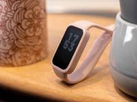 Un Xiaomi Smart Band 9 Active de color rosa que muestra la hora 17:53 sobre una superficie de madera junto a una taza decorada.