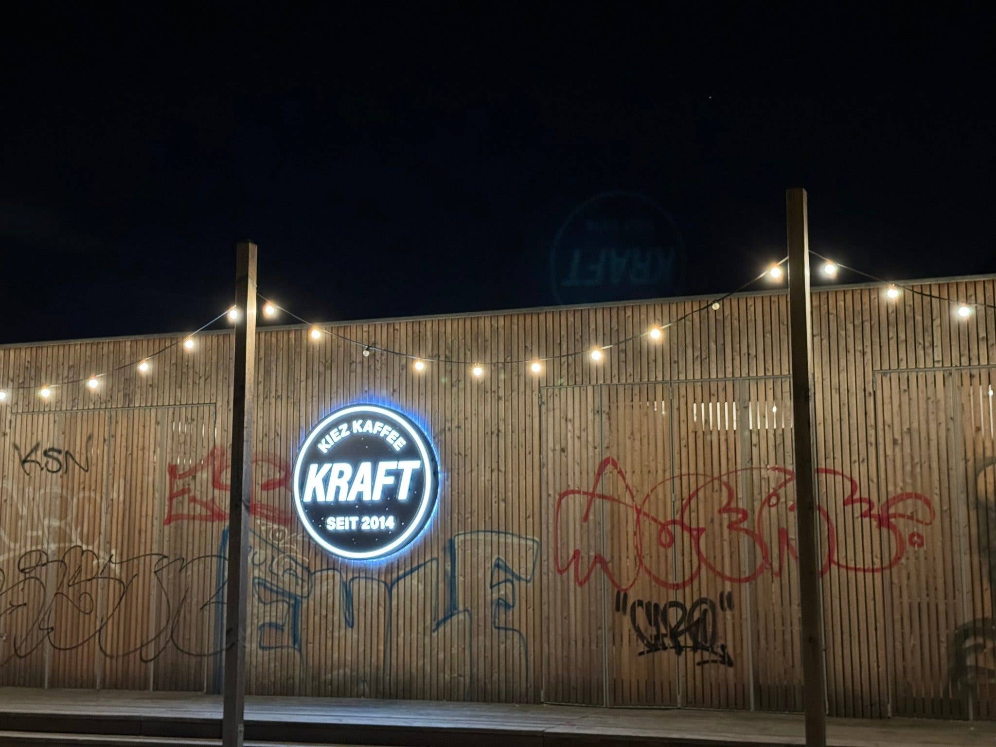 Photo prise avec l'iPhone 15 Pro Max de nuit de la devanture en bois d'un bar orné d'une pancarte circulaire et rétroéclairée