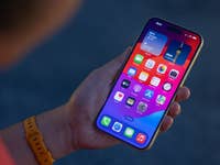 L'Apple iPhone 15 Plus vu de face tenu par Rubens dans sa main gauche dans la pénombre