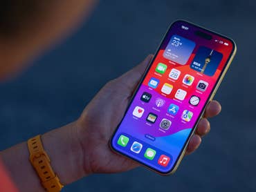 L'Apple iPhone 15 Plus vu de face tenu par Rubens dans sa main gauche dans la pénombre