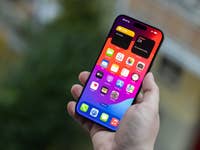 L'iPhone 15 Pro Max vu de face, tenu dans une main droite avec son écran allumé qui affiche l'écran d'accueil d'iOS 17