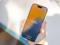 Une main tenant un Apple iPhone 16 Pro affichant un écran coloré avec 'bonjour'.