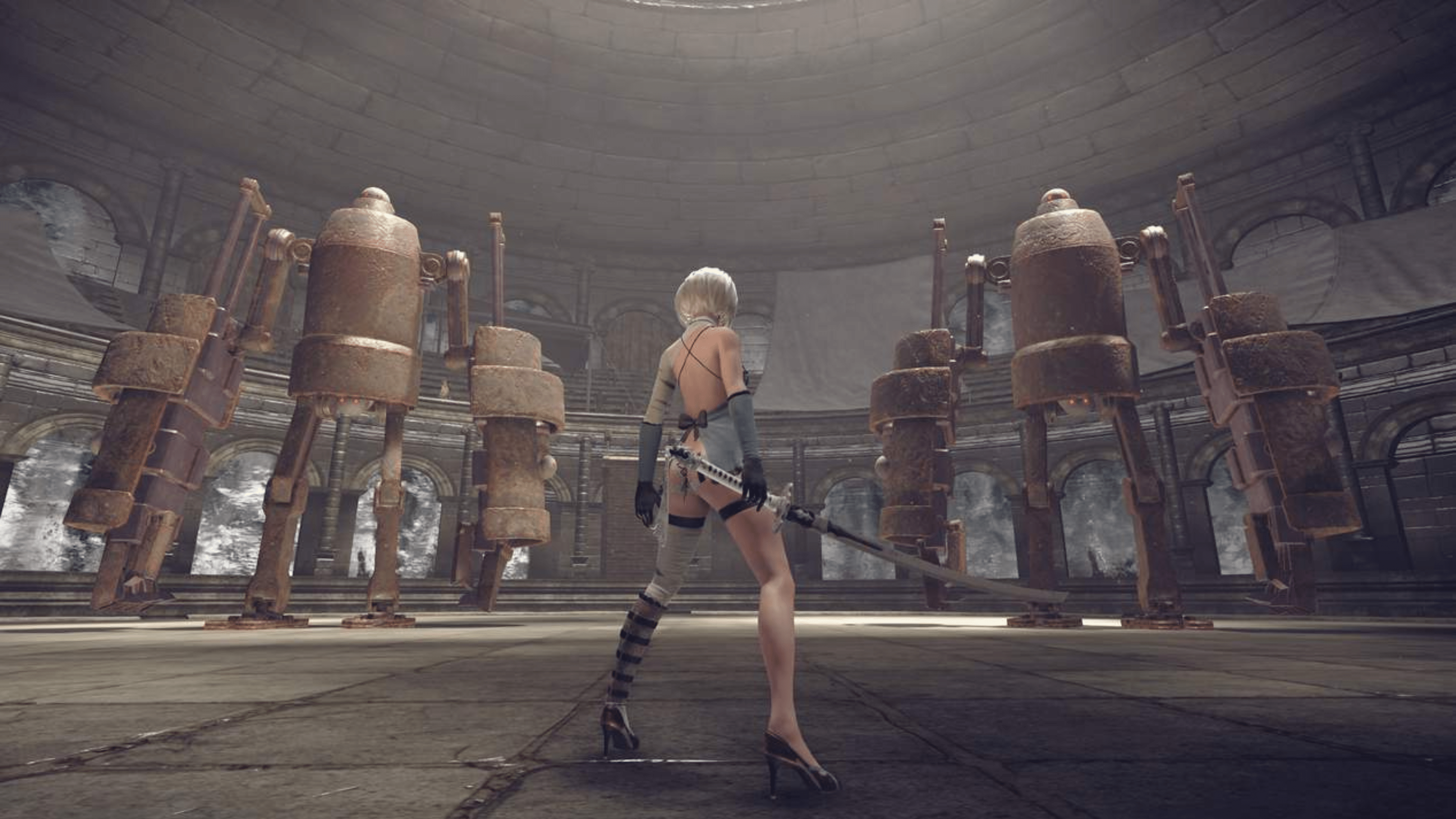 Un personnage de Nier: Automata se tient avec une épée dans une grande pièce circulaire avec des figures robotiques rouillées.