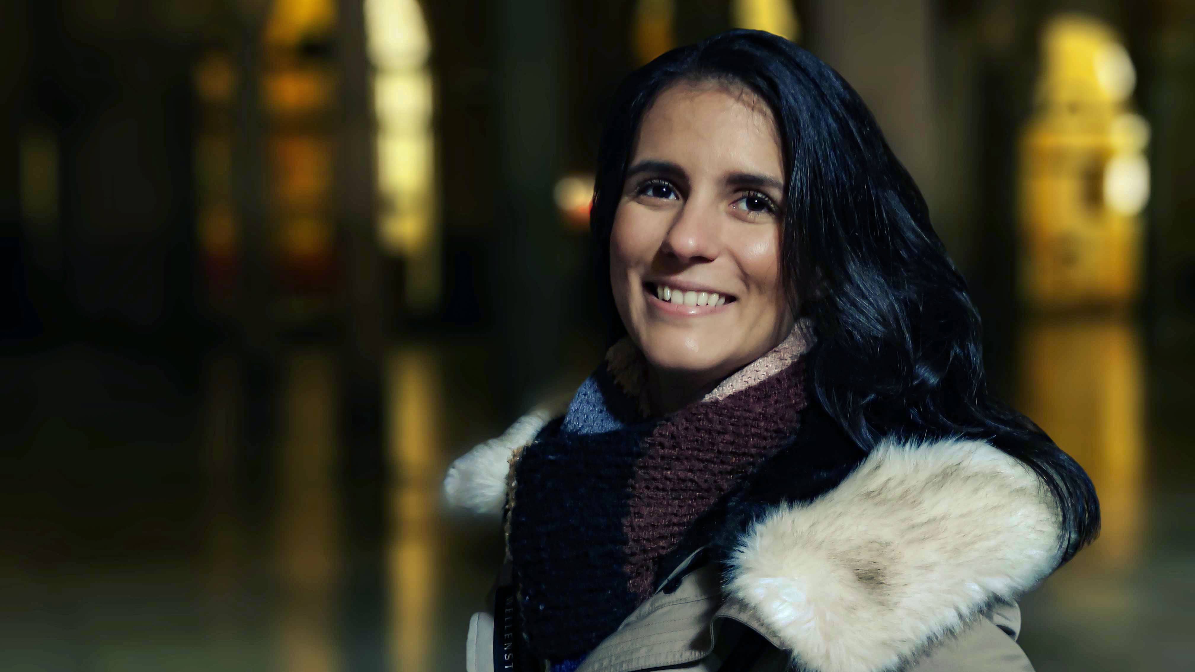 Une femme souriante en photographie nocturne, avec un éclairage doux et un fond flou.