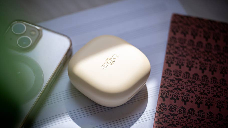 Un étui Shokz OpenFit 2 à côté du0027un smartphone sur des partitions et un cahier à motifs.