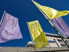 Drapeaux de Stellantis et Opel flottant contre un ciel bleu clair dans un lieu d'entreprise.