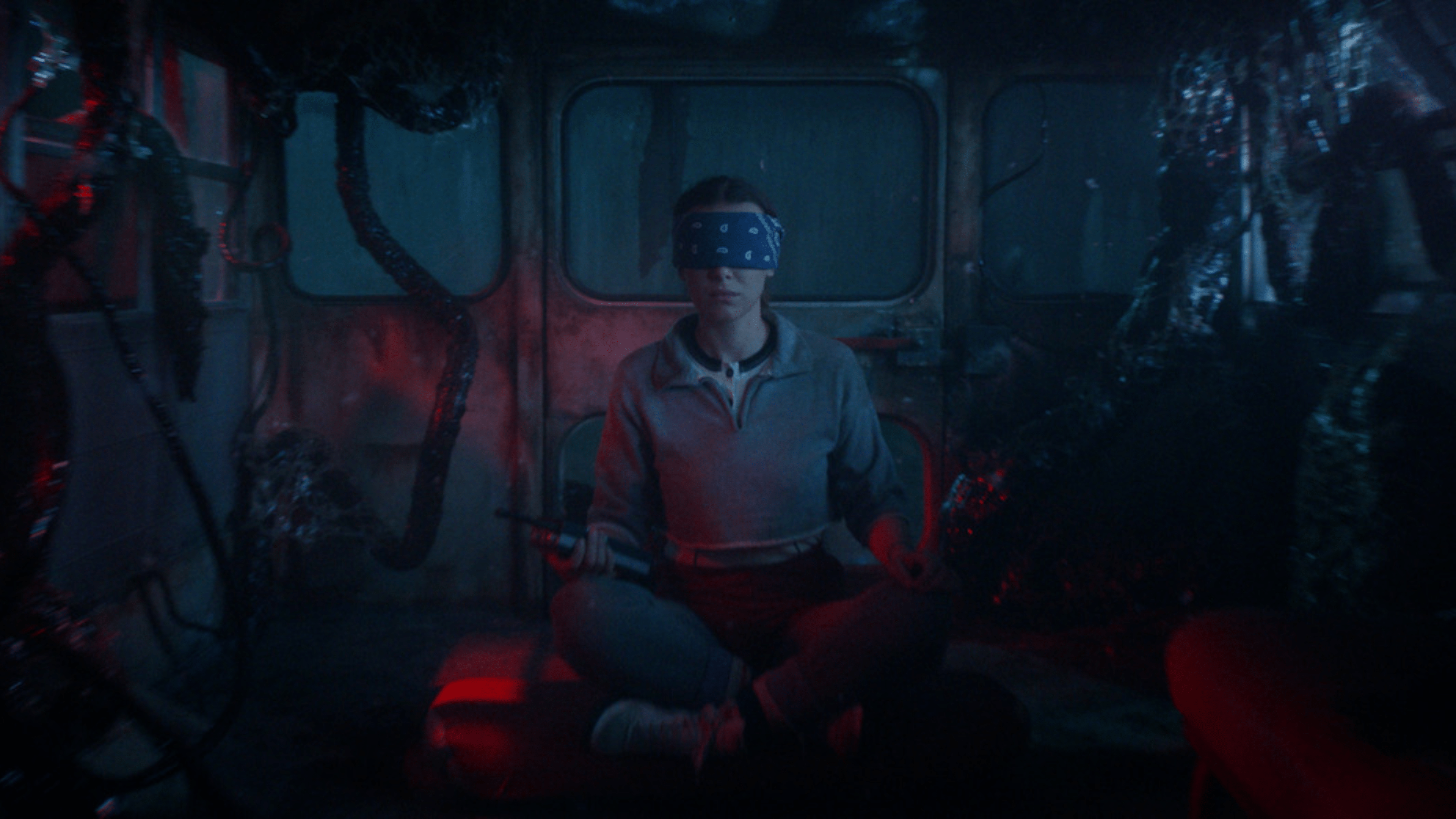 Une personne avec un bandeau sur les yeux est assise en tailleur dans un environnement sombre et mystérieux.