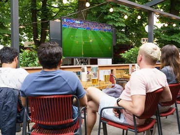 Groupe d'amis regardant un match de football sur un téléviseur extérieur Sylvox 4K dans un jardin.