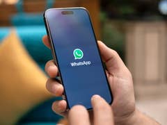 Une main tenant un smartphone affichant le logo WhatsApp à l'écran.