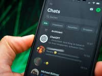Une main tenant un smartphone affichant un chat WhatsApp avec 'ChatGPT' et d'autres contacts.