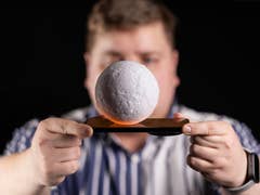 Un homme en arrière-plan tenant un Xiaomi 14 Ultra horizontalement à deux mains, les bras tendus, avec une boule blanche posée sur le smartphone au premier plan