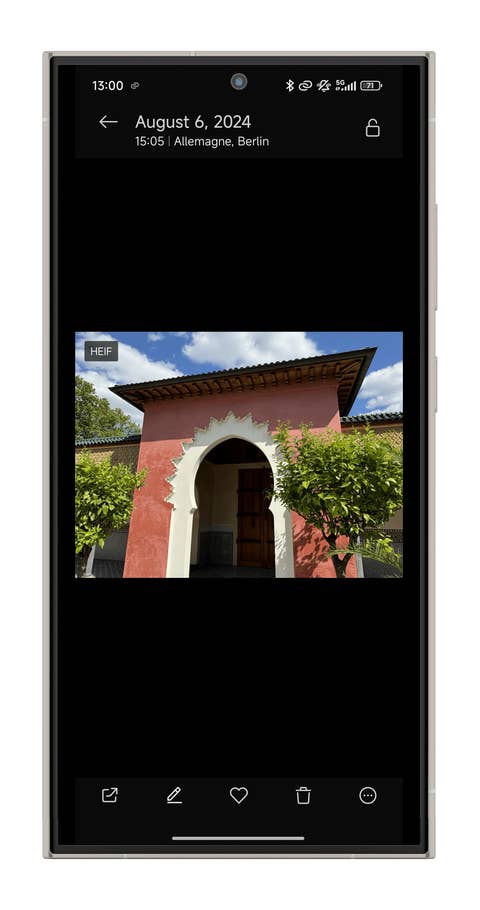 Un bâtiment coloré avec une arche et de la verdure, sous un ciel bleu avec des nuages.